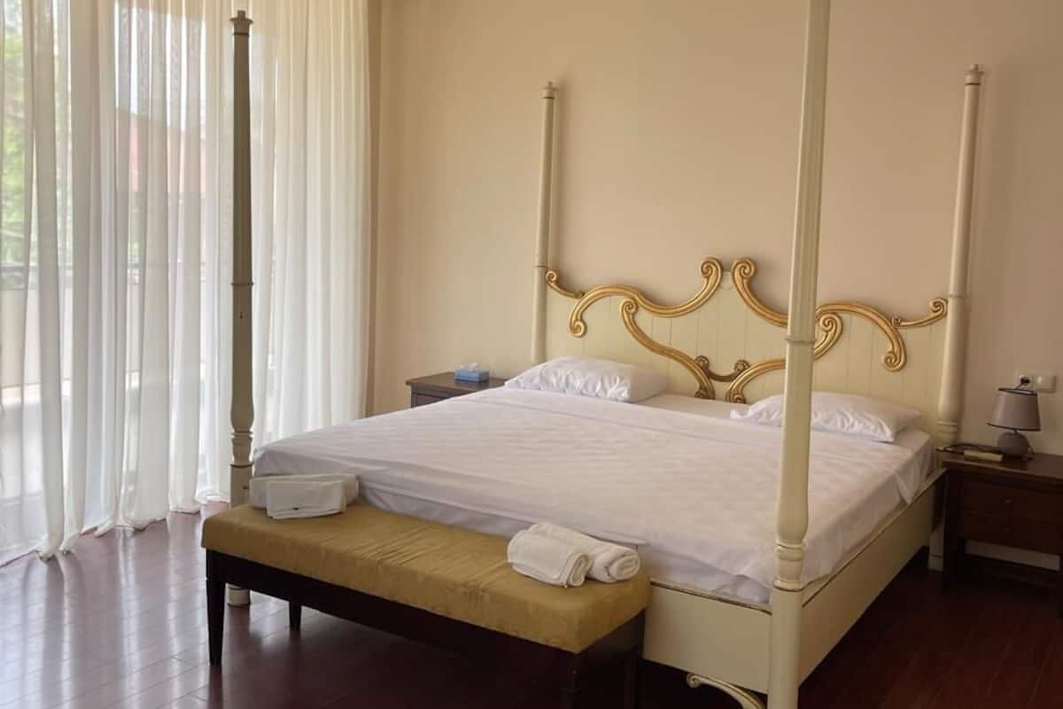 A four-poster bed with a wooden headboard, a bedside table, and a bench with a towel.