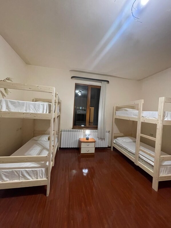 A room with two bunk beds, a small table with a lamp, a radiator, and a window with curtains. - Dreams House Hostel & Hotel (Yerevan)