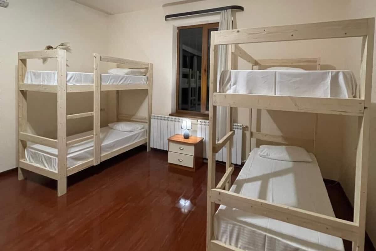 A room with two bunk beds, a small bedside table with a lamp, and a radiator.