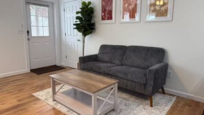 A living room with a grey sofa, a wooden coffee table, and a large plant. - Boone Adventure Hub: Spacious Studio Near Trails & Parkway (Boone)