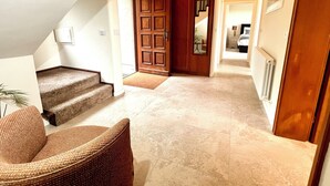 Ein Flur mit Holztür, Treppe und Korbsessel.
