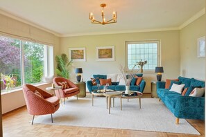 A spacious living room with a large window, a chandelier, and a teal sofa. - Tranquil 5-bedroom house on Caragh Lake, Co. Kerry (Co. Kerry V93N1F6)