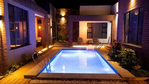 A rectangular swimming pool with a ladder, surrounded by a wooden deck and plants.