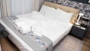 A neatly made bed with white linens, a bedside table with a lamp, and a floral-patterned headboard.