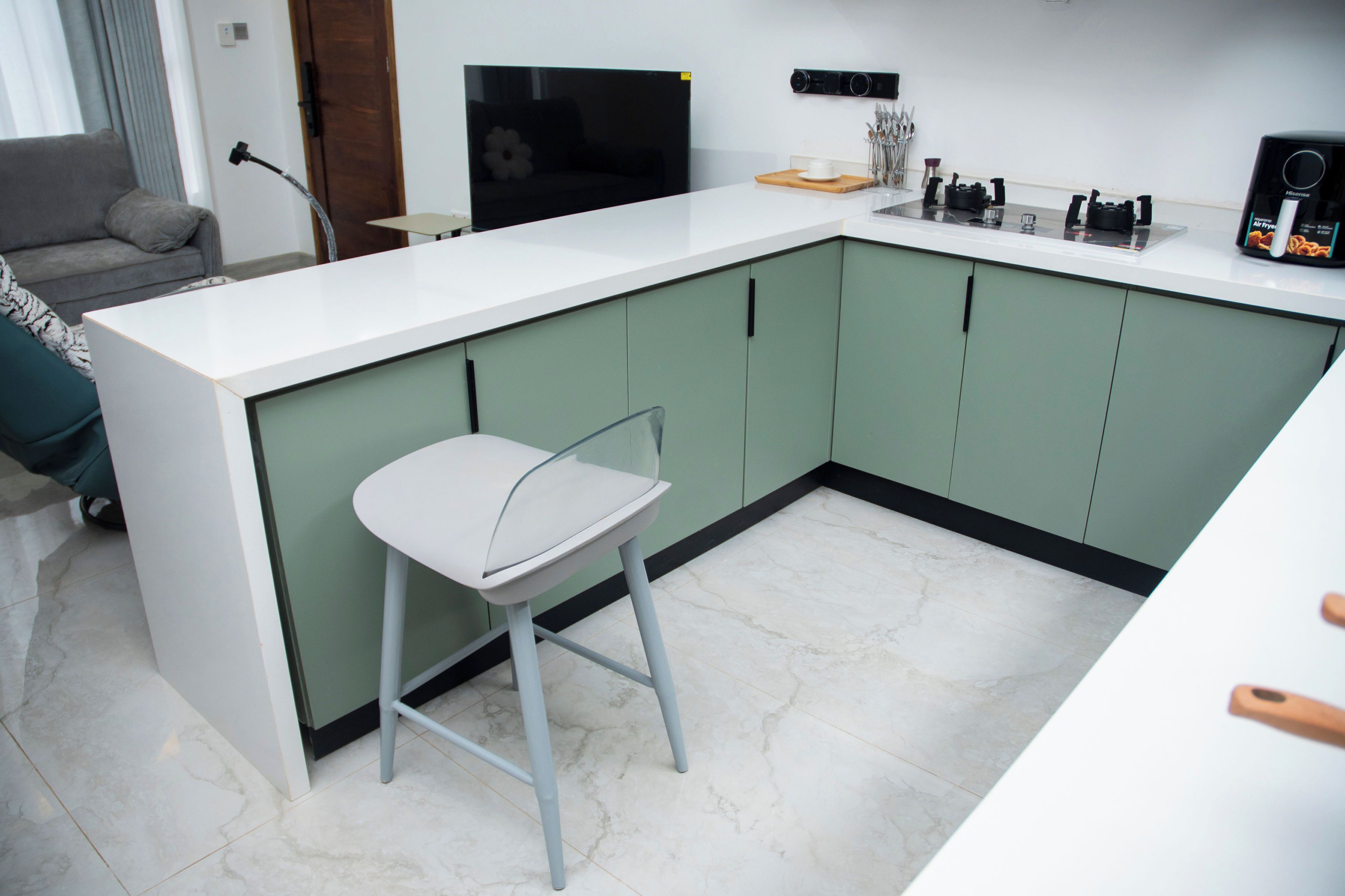 Een moderne keuken met een wit aanrecht, groene kastjes, een barstoel en een televisie.
