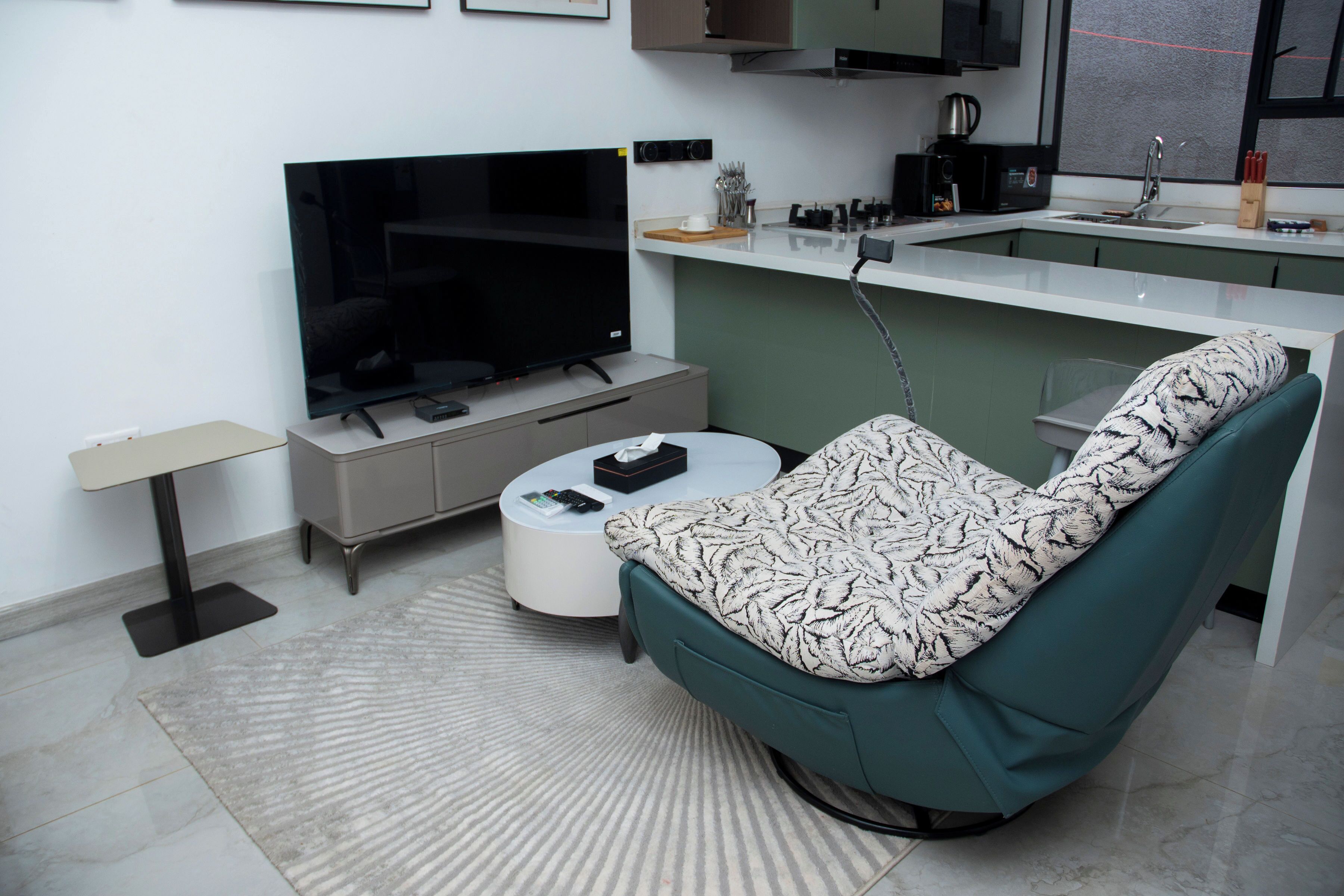 A modern living room with a flat-screen TV, a sofa, a coffee table, and a kitchen area in the background.