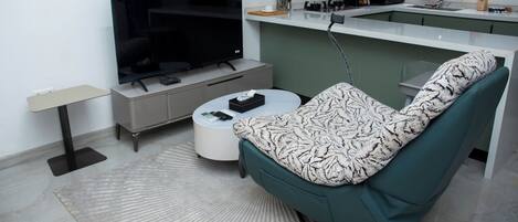 Een moderne woonkamer met een flatscreen televisie, een bank, een salontafel en een keuken op de achtergrond.