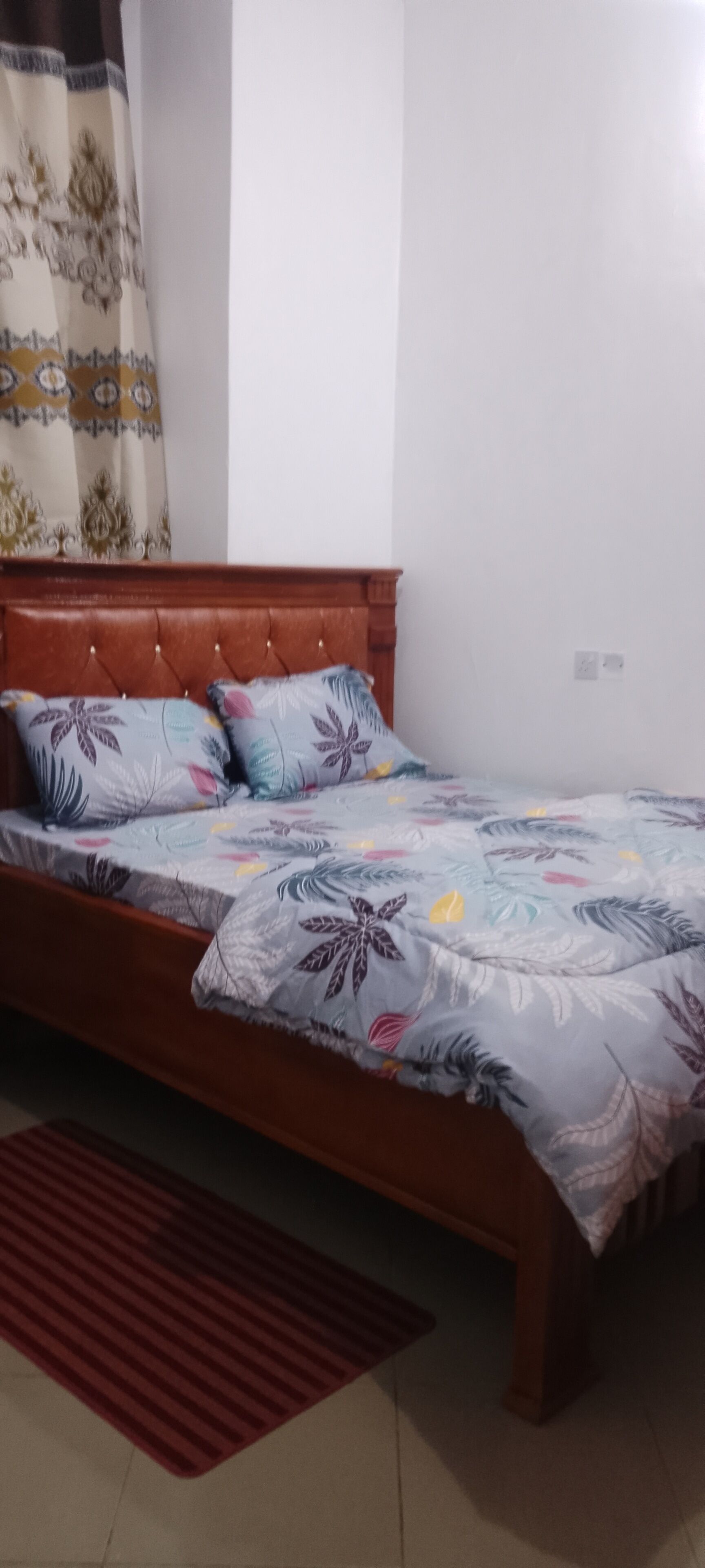 Una cama individual con una colcha de estampado floral, un cabecero de madera y una alfombra roja en el suelo.