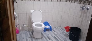 Ein Badezimmer mit einer weißen Toilette, einem blauen Kunststoffhocker, einem roten Eimer und einem schwarzen Eimer.