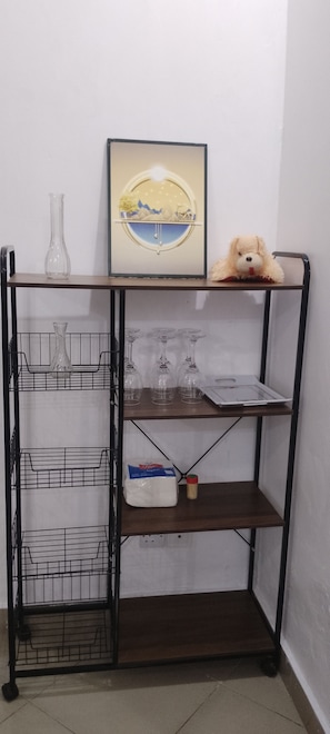 A metal shelf unit with multiple compartments, including a section with wine glasses and a section with a packaged item.