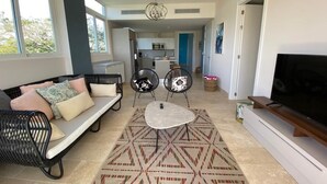 Una sala de estar con sofá, dos sillones, una mesa de centro, televisor y alfombra estampada.