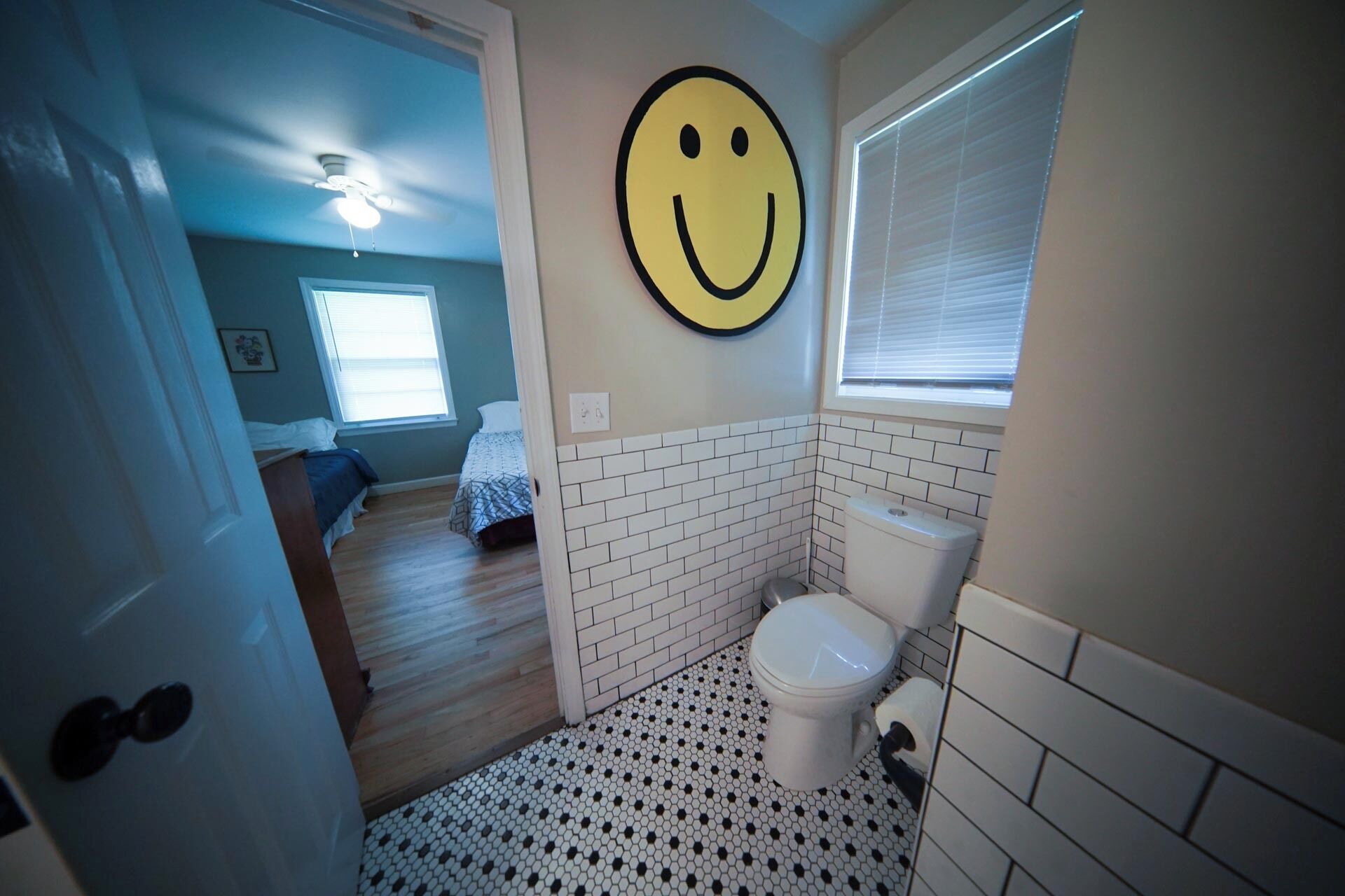 A bathroom with a toilet, a smiley face decoration, and a patterned floor.