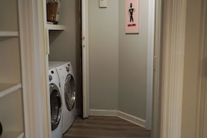 Una sala de lavandería con dos lavadoras de carga frontal y un estante encima.