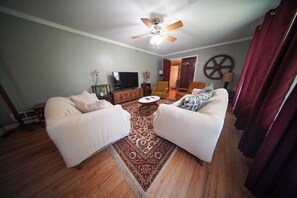 A living room with two sofas, a television, a ceiling fan, and a decorative wheel on the wall.