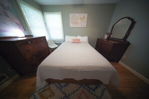 Un dormitorio con cama, cómoda, silla y espejo.