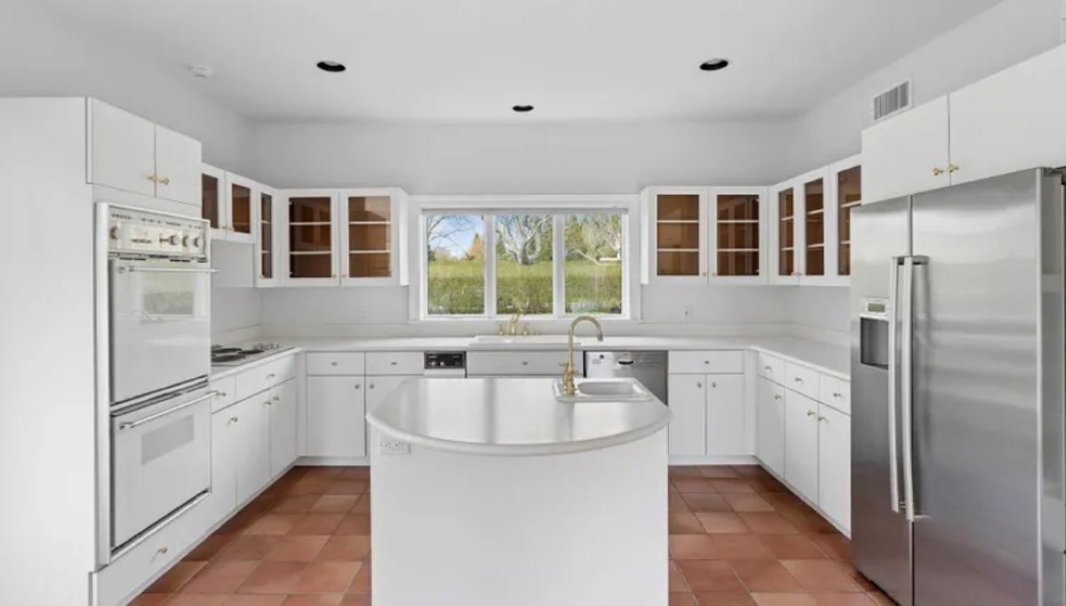 A modern kitchen with white cabinetry, a central island, stainless steel appliances, and a window providing a view of the outdoors.