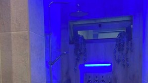 Een moderne badkamer met een douche, een houten wastafelmeubel en een plank met flessen.