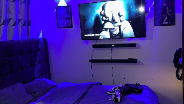 Een slaapkamer met een bed, een aan de muur bevestigde televisie en twee wandlampen.