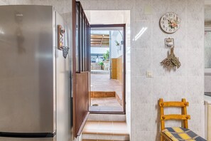 Uma cozinha com geladeira, uma cadeira de madeira, um relógio e um pequeno objeto decorativo na parede.
