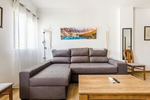 Uma sala de estar com um sofá seccional, uma mesa de centro de madeira, uma pintura de um lago montanhoso e um espelho na parede.