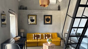 A modern living room with a yellow sofa, a wooden coffee table, a black metal chair, a dining table, and a black metal ladder. - THE L Lodge, Ocean View Private Garden Cottage (Tabua)