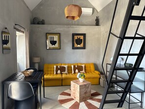 A modern living room with a yellow sofa, a wooden coffee table, a black metal chair, a dining table, and a black metal ladder. - THE L Lodge, Ocean View Private Garden Cottage (Tabua)