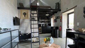 A modern interior with a loft bed, kitchen area, and a dining space. - THE L Lodge, Ocean View Private Garden Cottage (Tabua)