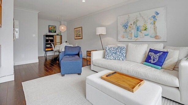Un salon moderne avec un canapé blanc, un fauteuil bleu et une table basse. Un tableau représentant des fleurs est accroché au mur.