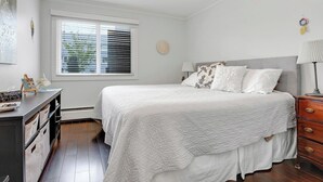 Une chambre à coucher comprenant un lit, des tables de chevet, une commode, une fenêtre avec des stores et un élément de décoration murale.