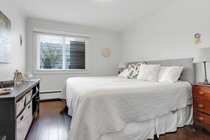 Ein Schlafzimmer mit Bett, Nachttischen, einem Schminktisch, einem Fenster mit Jalousien und einer Wanddekoration.