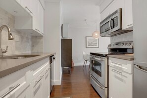 Een moderne keuken met roestvrijstalen apparatuur, witte kasten en een houten vloer.