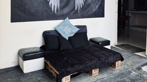A modern bedroom with a large wall-mounted artwork of white angel wings, a black sofa with patterned cushions, and a small bedside table.