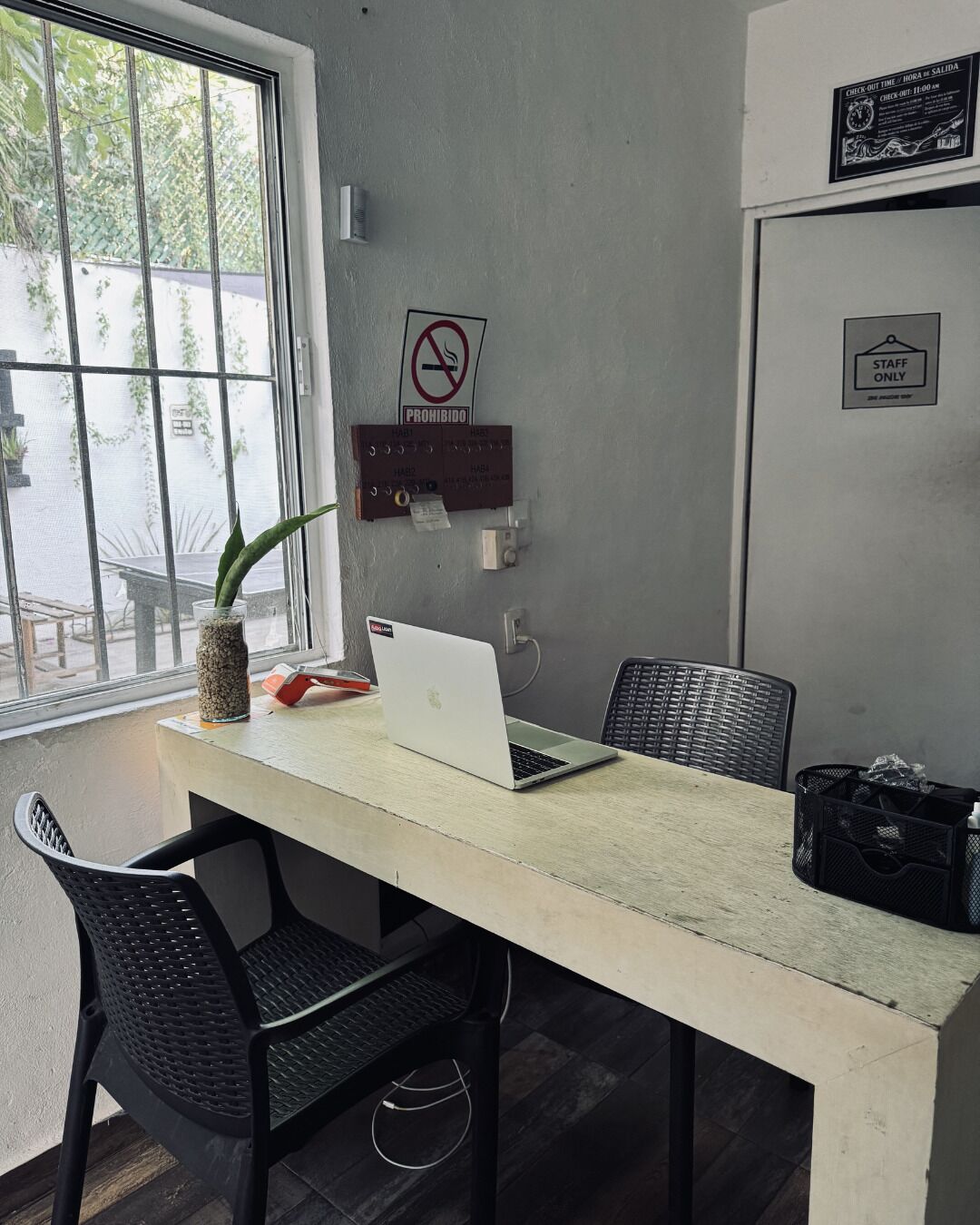 Un espacio de trabajo con una computadora portátil, un letrero de prohibido fumar, un letrero exclusivo para empleados y una ventana con plantas.