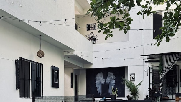 An outdoor seating area with tables and chairs, a black chair in the foreground, and a wall with a winged figure mural.