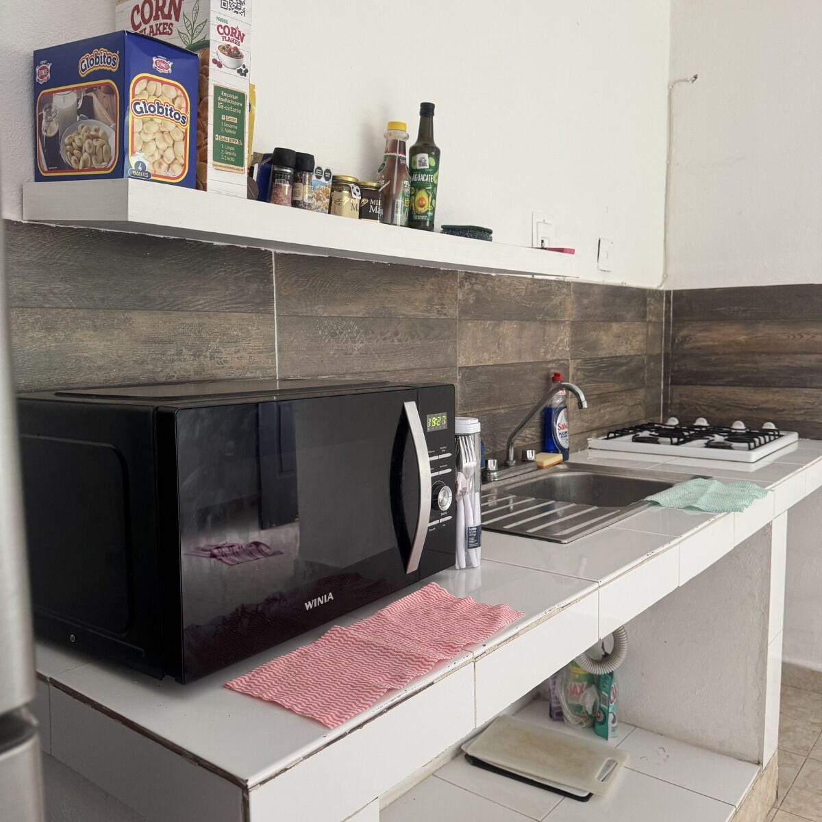 A kitchen with a black microwave, a sink, and various food items on the counter.