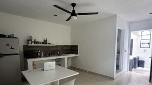 A kitchen with a white countertop, a ceiling fan, a refrigerator, and a dining area with a chair.