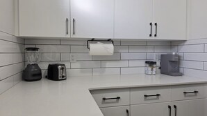 Uma cozinha com armários brancos, uma torradeira, um liquidificador e uma cafeteira.
