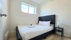 Um quarto com cama, mesa de cabeceira, janela e porta.
