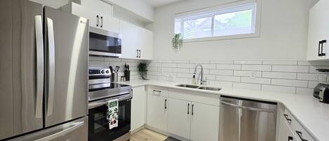 Een moderne keuken met roestvrijstalen apparatuur, witte kastjes, een raam en een kleine plant.