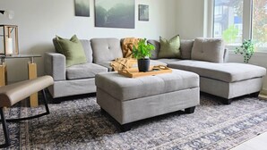 Un salon moderne avec un canapé d’angle gris, un banc, une table basse avec un plateau et une plante en pot.