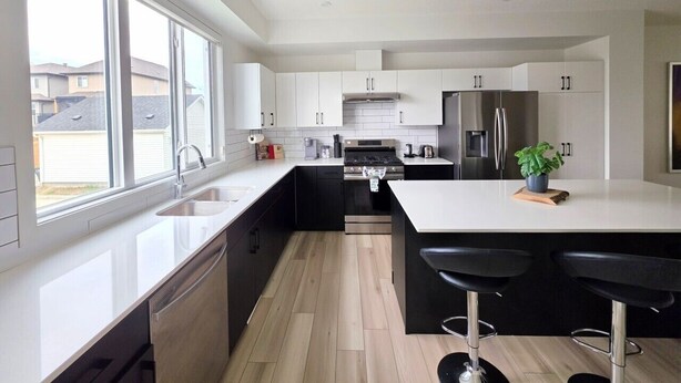 Une cuisine moderne dotée d’un grand îlot central, d’appareils électroménagers en acier inoxydable et offrant une vue sur le quartier.