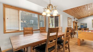 Un comedor con una mesa y sillas de madera, una araña y una mesa de futbolín.