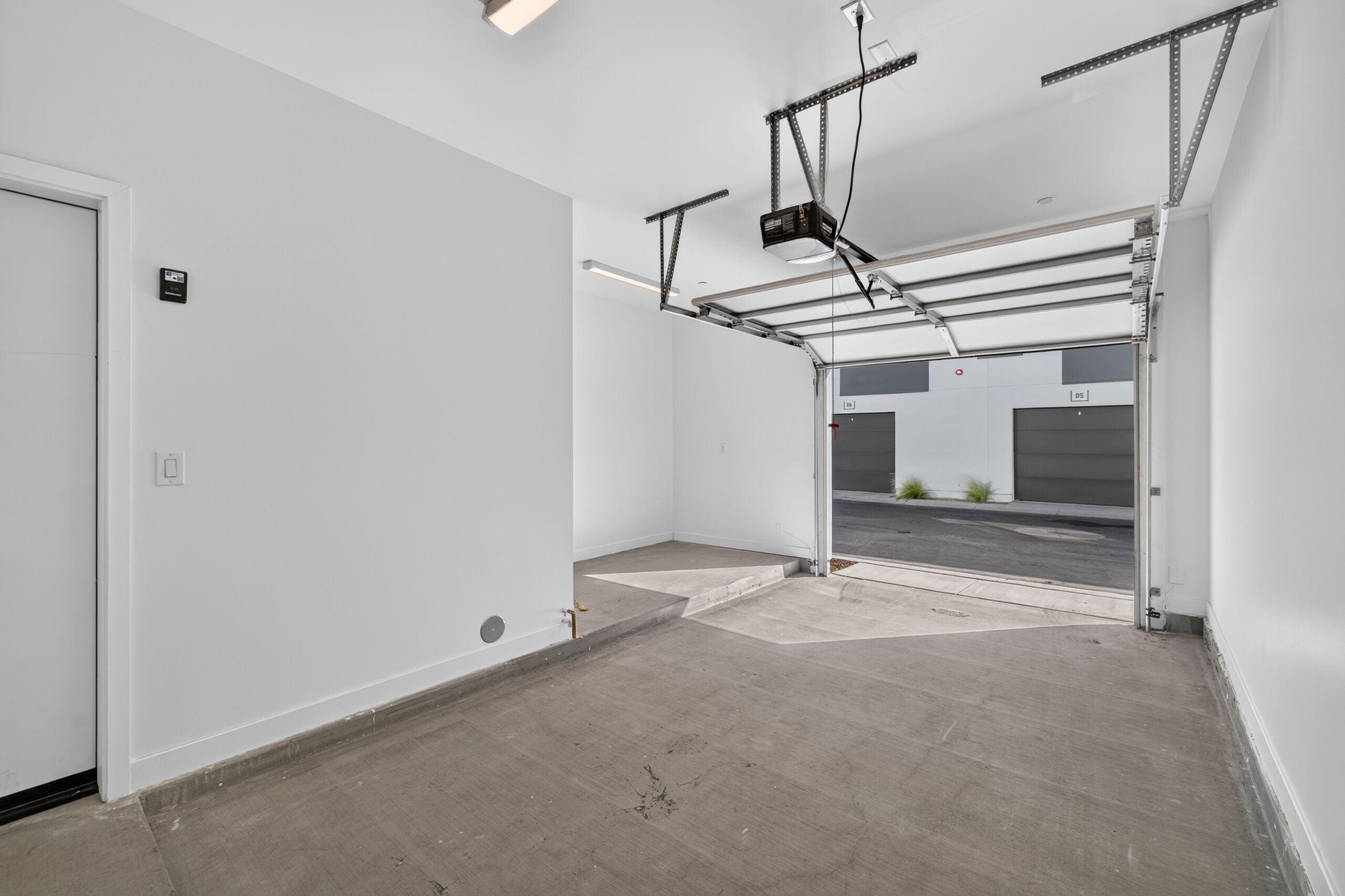 A clean, empty garage with a white door, a concrete floor, and a metal structure overhead.