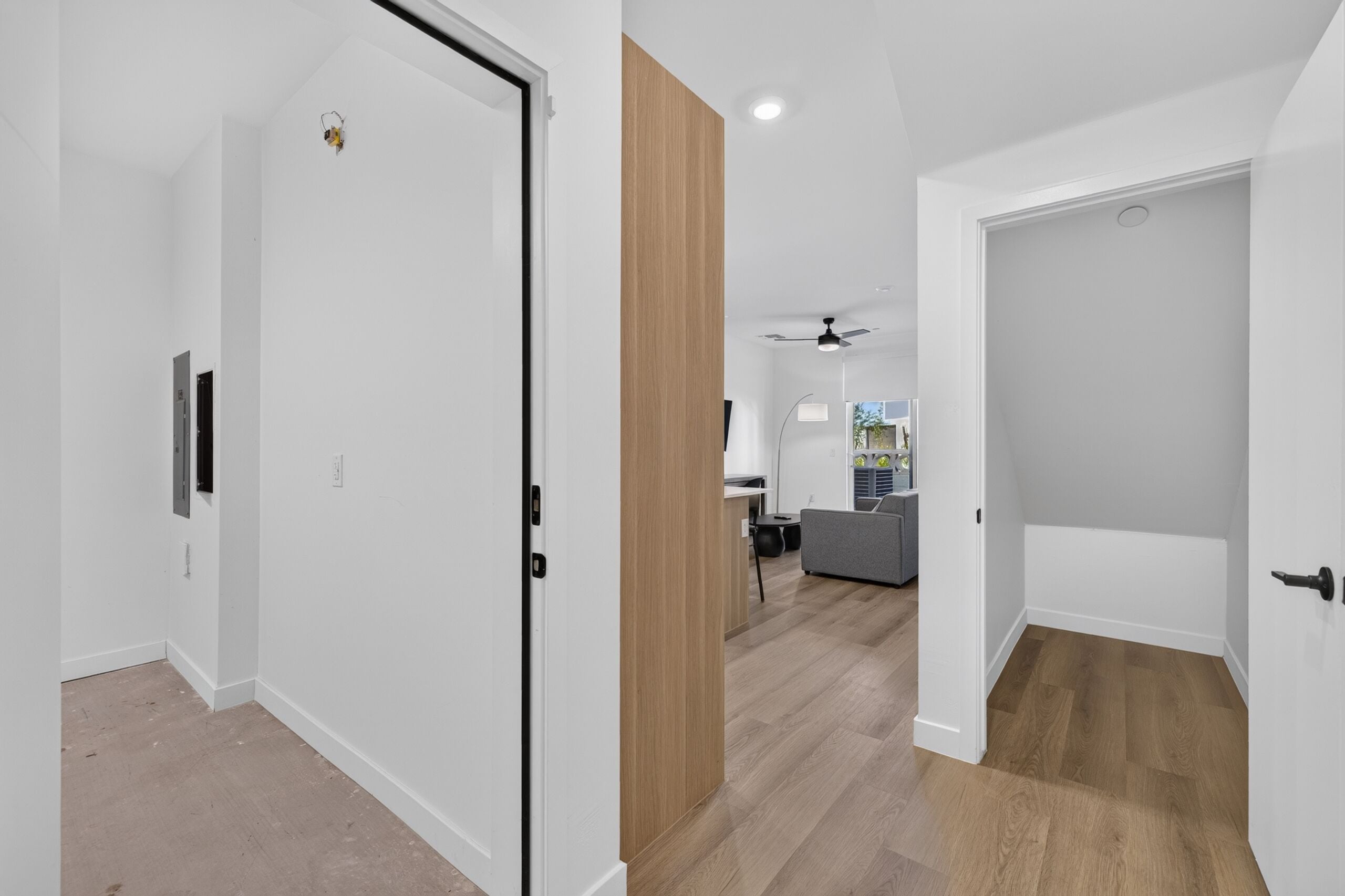 A modern interior with a hallway leading to a living area, a ceiling fan, and a visible kitchen area.