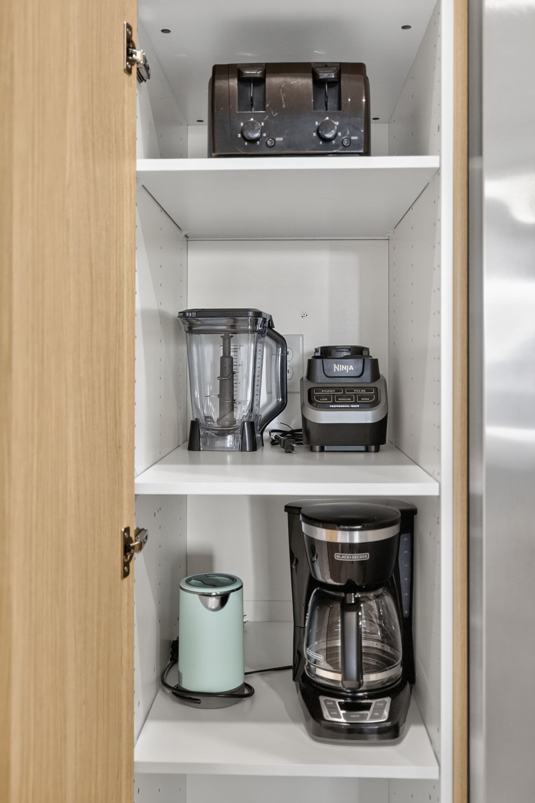 Cocina con tostadora, licuadora, cafetera y hervidor sobre estantes.