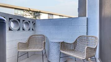 A balcony with two wicker chairs and a small round table, a concrete floor, and a grey wall with a circular design.