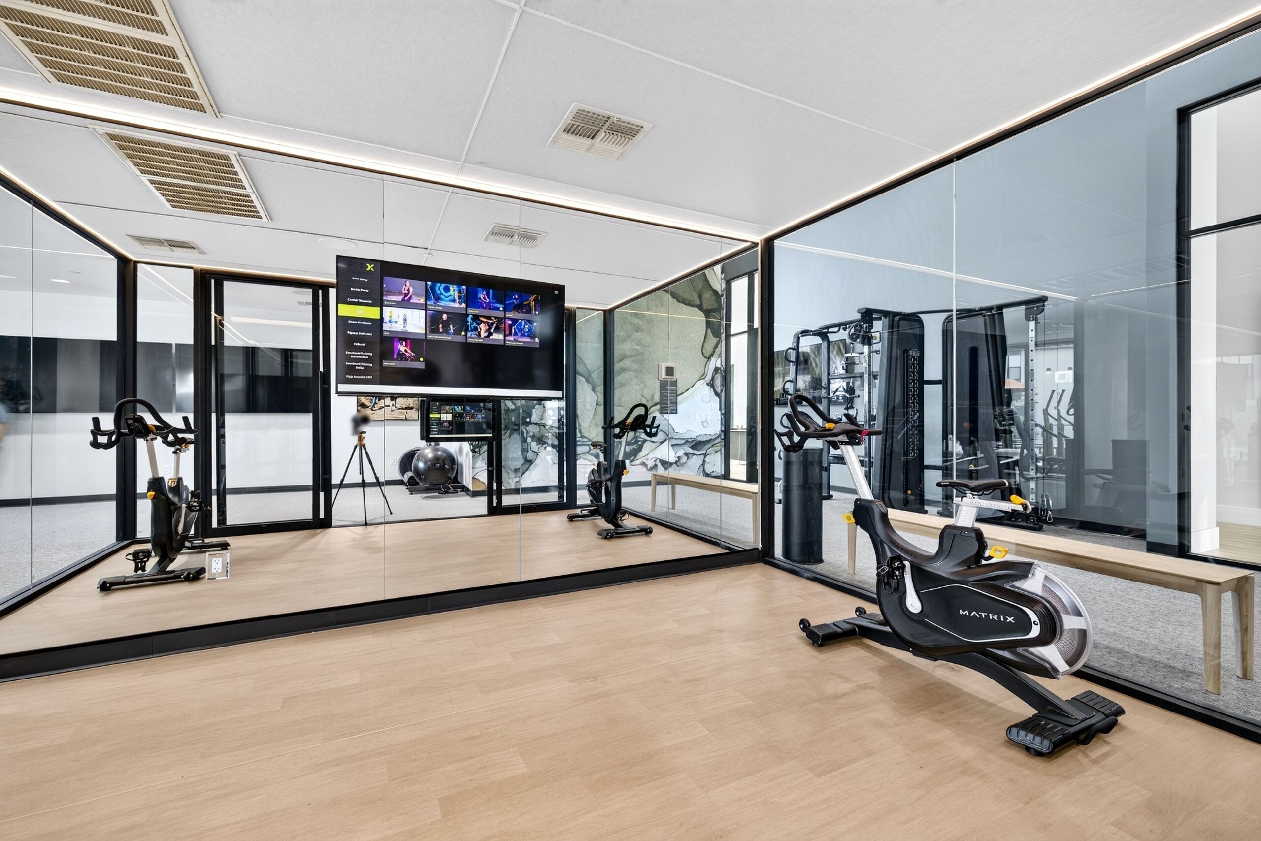 A modern gym with cardio machines, a TV screen, and a large mirror.