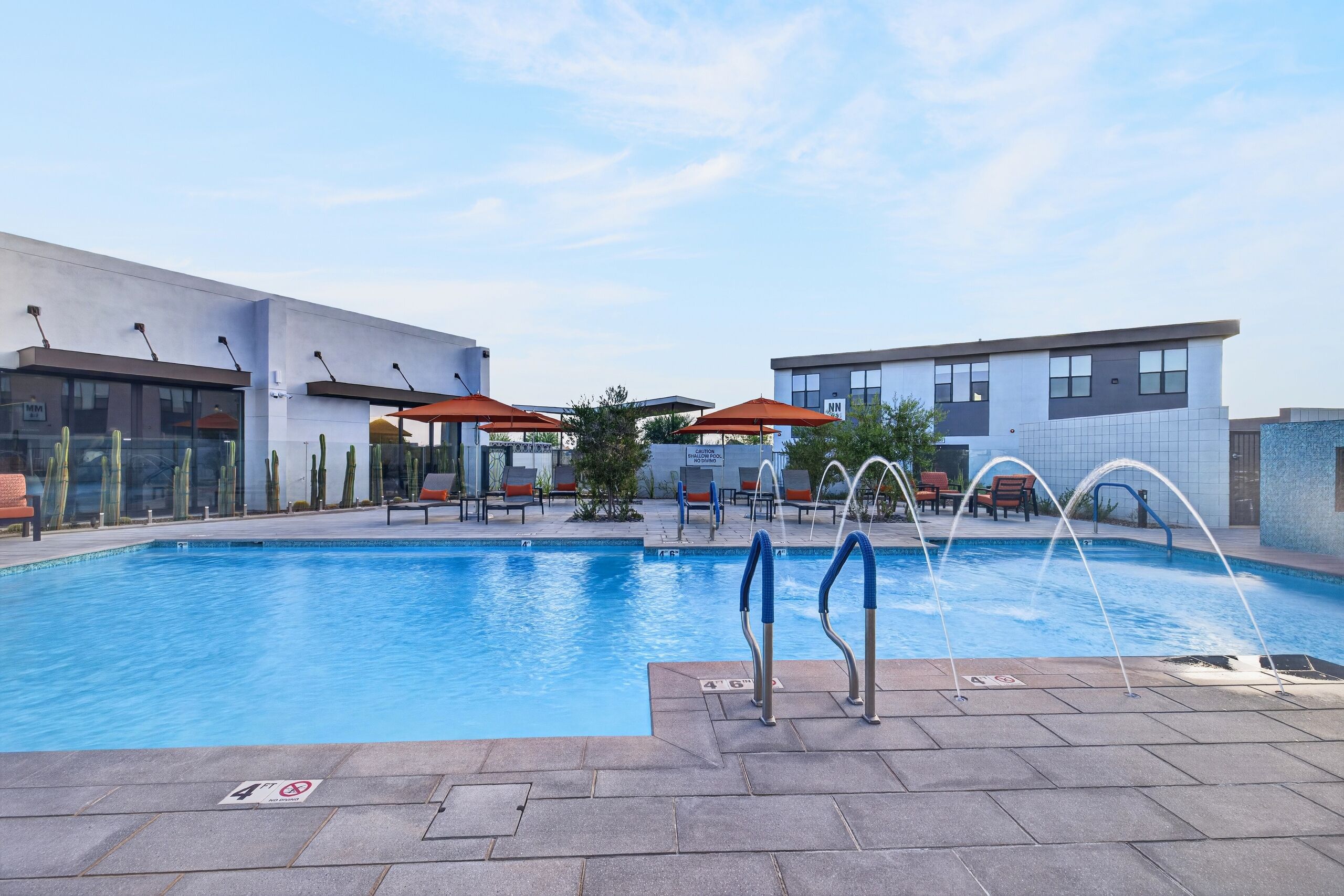 Ein Pool mit Liegestühlen und Sonnenschirmen, ein Gebäude mit modernem Design und ein klarer Himmel.