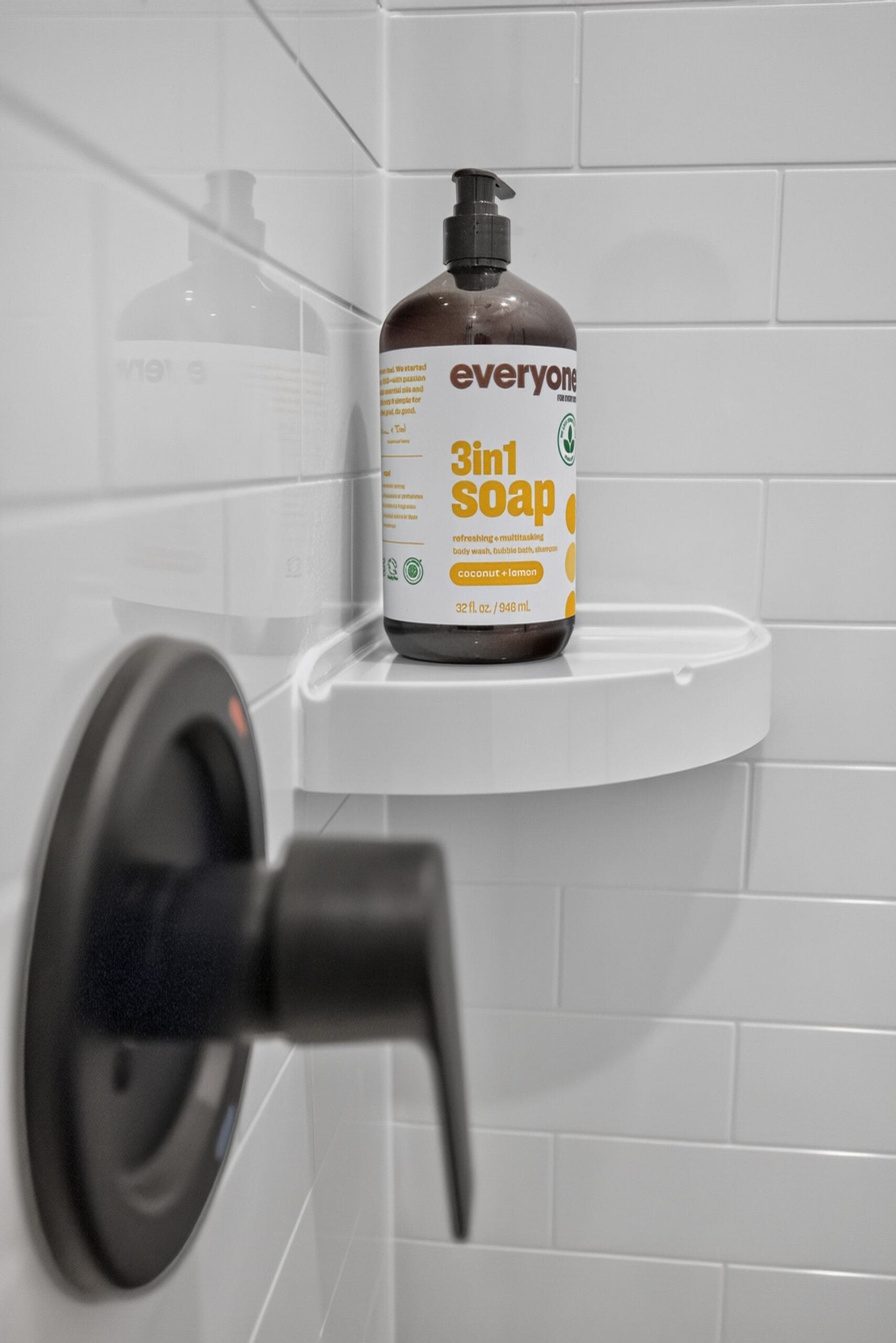 A bathroom with a white tiled wall, a white sink, and a bottle of 3in1 soap on the sink.