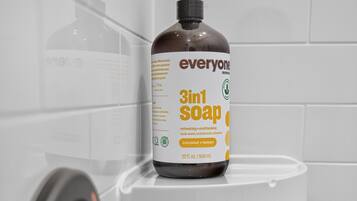 A bathroom with a white tiled wall, a white sink, and a bottle of 3in1 soap on the sink.